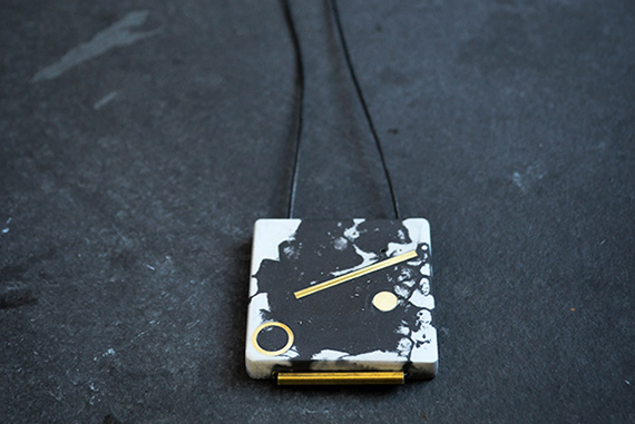 Pigmented concrete necklace with brass inlay hung from a black leather cord.