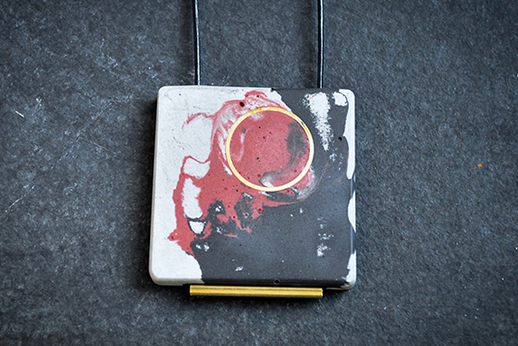 Black and red pigmented concrete necklace with brass inlay on a black leather cord.